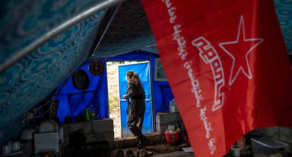 Red flag in foreground. Female soldier walking out of tent.